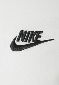 Fehér szövet, fekete hímzett Nike logóval; a logó egy stilizált swoosh-ot és a "NIKE" szót tartalmazza vastag, sans-serif betűtípussal.