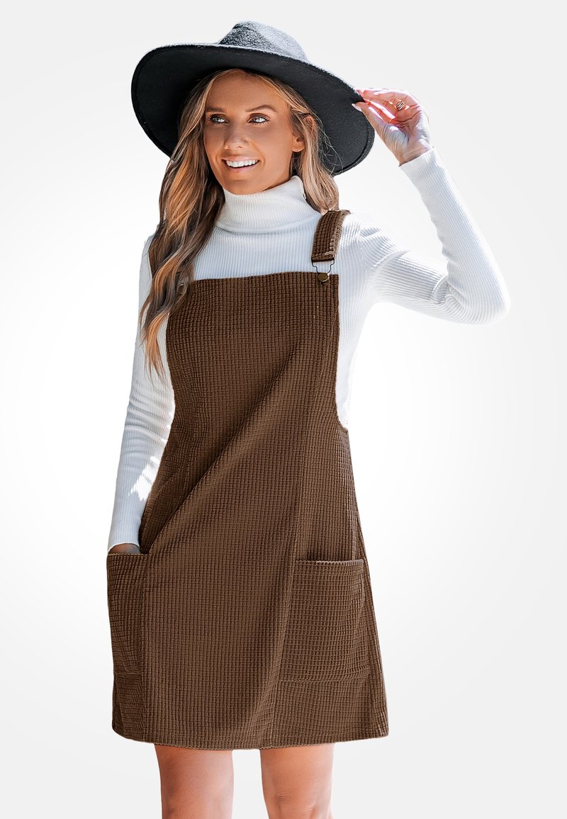 Robe salopette en velours côtelé marron avec bretelles ajustables, deux poches avant, portée sur un col roulé blanc. Texture lisse avec un motif en grille.