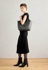 Black leather tote bag with a geometric pattern, featuring a keychain detail. The bag has a wide opening and sturdy handles.