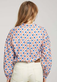 Chemise à manches longues avec un motif de formes en goutte d'eau bleues et orange sur un fond blanc. Tissu doux et coupe ample.