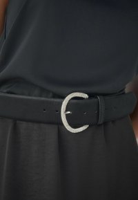 Czarny pasek z gładkiej skóry z błyszczącą, srebrną klamrą, na której znajduje się elegancka, zakrzywiona ozdoba z kryształków.