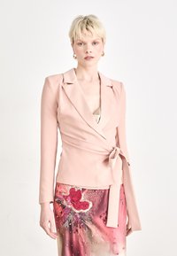 Blush rosa omslagsblazer med rever og knyttet midje, parret med et m�ønstret skjørt som har blomsterbroderi og paljetter.