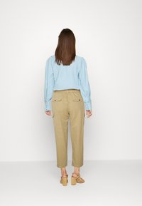 Blusa azul clara com mangas bufantes, calças cargo bege com cintura ajustável por cordão e bolsos laterais, acompanhadas de sandálias de salto bloco em tom bege.