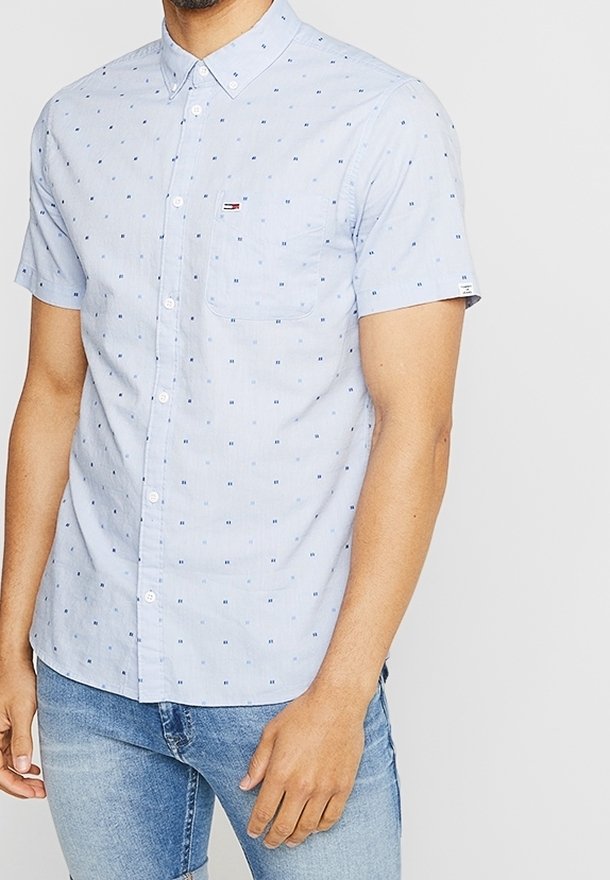 Světle modrá košile s krátkým rukávem a knoflíkovým zapínáním, s malými modrými čtvercovými vzory, náprsní kapsou a logem Tommy Hilfiger, v kombinaci s džíny.