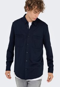 Marineblå skjorte med knapper foran laget av mykt stoff, med to brystlommer, klassisk krage og lange ermer med knappede mansjetter.