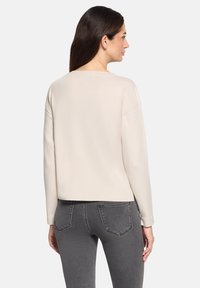 Jasno beżowy sweter o luźnym kroju, z miękkiego materiału, z szerokim dekoltem i opuszczonymi ramionami. Połączony z ciemnoszarymi dopasowanymi dżinsami.