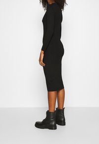 Robe midi noire en tricot avec manches longues, texture côtelée, design ajusté, associée à des bottines noires à lacets.