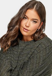 Stickad tröja i mörkgrön med texturerade ränder, med vida ärmar och rund halsringning. Tyget har en mjuk och bekväm känsla.