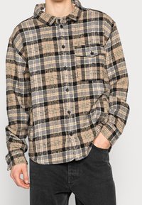 Rutigt button-up skjorta i mjukt material, med beiga, svarta och grå färger, framfickor och rundad nederkant.