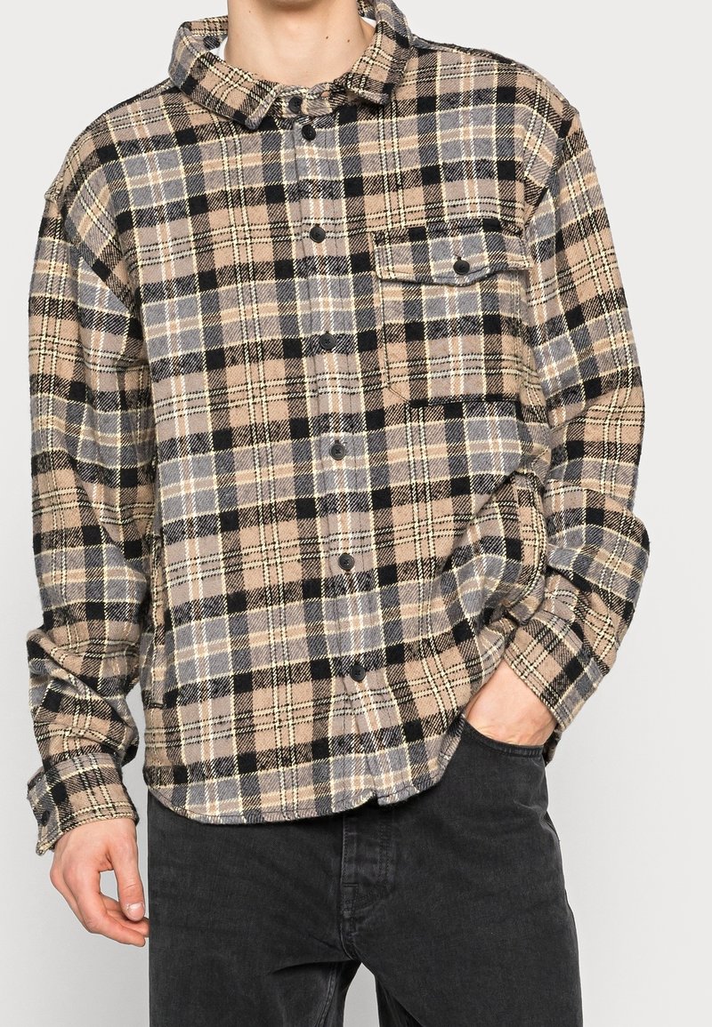 Rutigt button-up skjorta i mjukt material, med beiga, svarta och grå färger, framfickor och rundad nederkant.