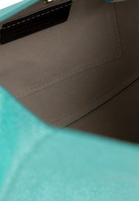Interno della borsa in pelle turchese, texture liscia, fodera marrone, cuciture prominenti, etichetta con la scritta "Made in Italy". Spazio aperto visibile.