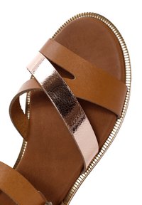 Sandal in pelle marrone con cinturini larghi, uno dei quali presenta un accento in metallo testurizzato. Rifinita con un bordo dorato. Suola liscia.