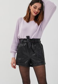 Un pull en lilas tricoté avec des manches amples, accompagné de shorts en faux cuir noir taille haute avec une ceinture à nouer. Texture lisse et design ajusté.