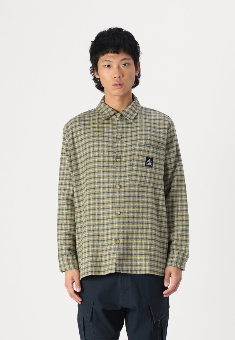 Green and beige checkered shirt with a button-up front, collar, long sleeves, and a chest pocket featuring a branded patch.