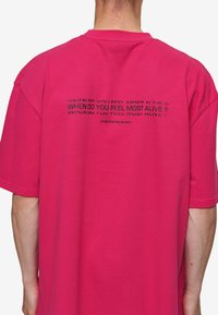 Pink oversized t-shirt featuring black text on the back that reads "WHEN DO YOU FEEL MOST ALIVE?" with "PEGBOARD" beneath it.