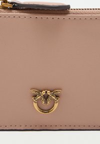 Ροζ δερμάτινο πορτοφόλι με χρυσό τόνο και σχέδιο πουλιού. Λείο υλικό, κλείσιμο με φερμουάρ και αντίθετη μαύρη ραφή.