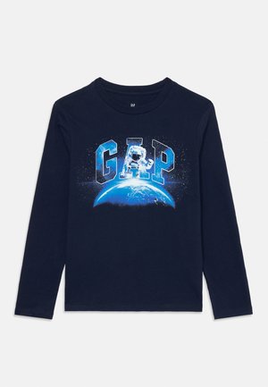 Chemise à manches longues marine avec le logo GAP, mettant en avant un astronaute et un graphique de la Terre dans des couleurs bleues et blanches.