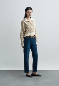 Beige knitted sweater with a white collar and half-zip, paired with dark blue straight-leg jeans. Black flats complete the outfit.