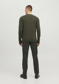 Sweater en tricot vert foncé avec un col rond et des poignets côtelés, associé à un pantalon noir texturé et des chaussures noires, vu de l'arrière.