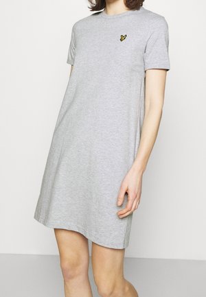 Vrouw draagt een lichtgrijze casual jurk met korte mouwen en een klein geel vogel-logo op de bovenkant van de linkerborst, staand tegen een effen witte achtergrond.