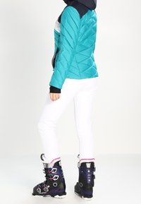 Turkusowa kurtka puchowa z haftem w zygzak, czarnym kapturem oraz białymi i szarymi akcentami. Noszona na białych spodniach i czarnych butach narciarskich z fioletowym wykończeniem.