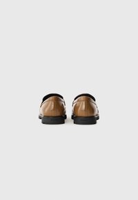 Chaussures en cuir verni marron avec un design épuré, des bouts ronds et une semelle en caoutchouc noir basse. Logo de la marque embossé sur le talon.