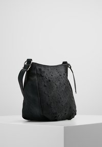 Bolso de ante negro con un diseño floral en relieve, forma curvada y una correa de hombro ajustable. Textura suave con acentos sutiles.