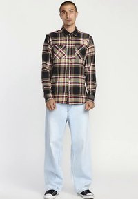 Sort og gul ternet skjorte med knappelukning og to brystlommer, kombineret med lyseblå vide jeans og sorte sneakers.