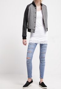 Szary sweter bomber z czarnymi rękawami, tank top z koronkowym wykończeniem w białym kolorze, podarte jasnoniebieskie dżinsy oraz czarne buty wsuwane.