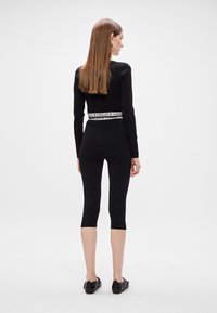 Crna majica dugih rukava i tajice s brendiranim pojasom. Glatka tekstura, uski kroj i skraćena dužina nogavica. Jednostavno i monochromatski.