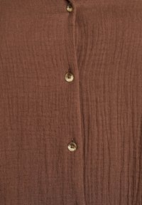 Brown textured fabric with vertical lines features three round, light-colored buttons along the front.
