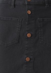 Temno modra denim krila z zapiranjem na sprednje gumbe, dvema sprednjima žepoma in rjavimi kovinskimi gumbi. Tkanina ima gladko teksturo.