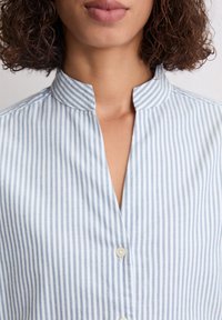 Lichtblauwe en witte gestreepte shirt met een Mandarin kraag, uitgerust met een knoopsluiting, een gladde textuur en een verticaal streepjespatroon.
