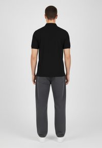 �Černé polo tričko s krátkými rukávy, doplněné volnými šedými kalhotami a bílými teniskami. Prostředí má neutrální pozadí.