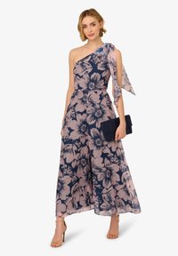 Bloemen jumpsuit met een schouderontwerp, marineblauwe en roze kleuren, doorschijnende textuur en een vloeiende silhouet. Gecombineerd met een marineblauwe clutch.