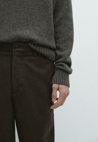 Szary dzianinowy sweter z prążkowanymi mankietami w połączeniu z ciemnobrązowymi spodniami z pojedynczym zapięciem na guzik i subtelną fakturą.