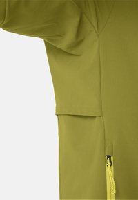 Gros plan sur un tissu vert olive avec une couture et une tirette de fermeture éclair jaune avec un cordon attaché en bas à droite.