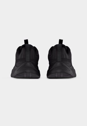 Paire de baskets de sport noires vues de dos, avec languettes de traction et semelles épaisses et texturées sur un fond gris uni.