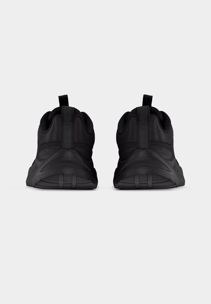 Paire de baskets de sport noires vues de dos, avec languettes de traction et semelles épaisses et texturées sur un fond gris uni.