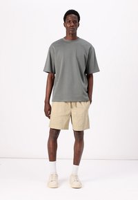 Graues Kurzarm-T-Shirt aus weichem Stoff, kombiniert mit beigen Leinen-Shorts und hellen Sneakers, auf einem schlichten Hintergrund präsentiert.