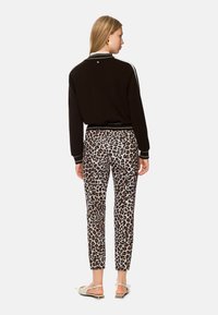 Black sweater with white cuffs and trim, paired with beige pants featuring a leopard print. Model wears light-colored flats.