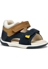 Sandalia de ante navy y beige con diseño de punta abierta, tira de Velcro, acento amarillo y suela de goma blanca. Presenta agujeros de ventilación para mayor transpirabilidad.