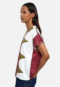 T-shirt z dekoltem w serek, wykonany z miękkiego materiału, z abstrakcyjnym wzorem w kolorach bordowym, białym i oliwkowym, krótki rękaw oraz luźny krój.