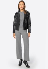 Chaqueta de biker de cuero negro con cremallera asimétrica, suéter de punto gris, pantalones de pierna ancha grises y botas de tobillo negras con tacón.