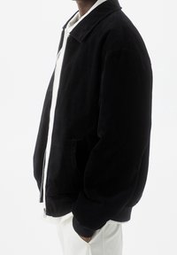 Giacca in corduroy nera con zip frontale, colletto ampio e tasche laterali. Le maniche sono leggermente bufanti e la texture è morbida.
