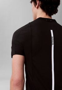 Ung person sett bakfra iført svart mesh treningsskjorte med vertikal hvit stripe og "Calvin Klein"-tekst på baksiden.