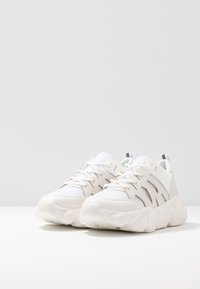 White athletic shoes with mesh panels, gold accents, and textured rubber soles. Features a padded collar and laces for secure fit.