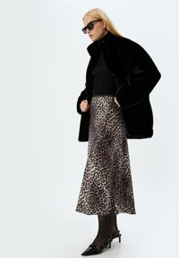 Abrigo de piel sintética negro sobre un top negro de canalé y una falda midi de estampado de leopardo. Tacones negros con una punta pequeña y afilada.