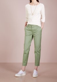 Maglione bianco a tre quarti con scollatura tonda, abbinato a pantaloni tapered verdi chiari e sneakers bianche.
