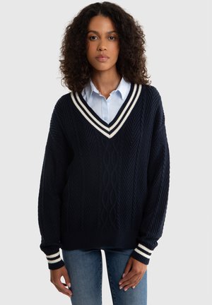 Granatowy, oversize sweter z dekoltem w serek, z białymi i kremowymi paskami, teksturowanym wzorem w warkocz oraz prążkowanymi ściągaczami w paski.